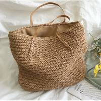 Große beige Strohtasche mit Ledergriffen, ideal für Strand oder Einkauf, auf weißem Hintergrund.