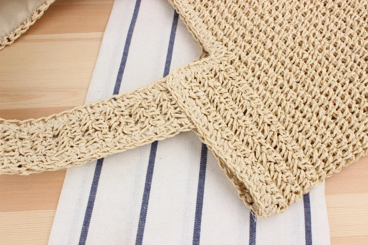 Beige gehäkelte Einkaufstasche aus Baumwolle auf gestreiftem Stoffhintergrund.