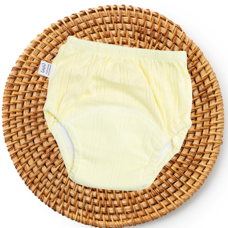 Gelbe Babyunterhose aus Baumwolle auf rundem geflochtenem Korb, weiches und atmungsaktives Material.