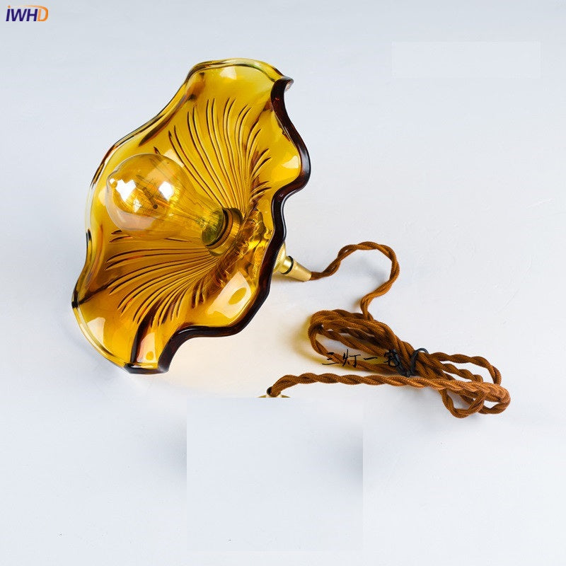 Gelbe Vintage-Lampe aus Glas mit geschwungenem Design und braunem Kabel für Retro-Einrichtung.