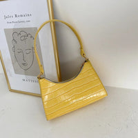 Gelbe Krokodilleder-Handtasche vor Kunstposter, modisches Accessoire, elegantes Design.