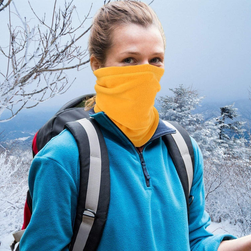 Frau mit gelbem Fleece-Schal und blauem Pullover beim Wandern im verschneiten Winterwald.