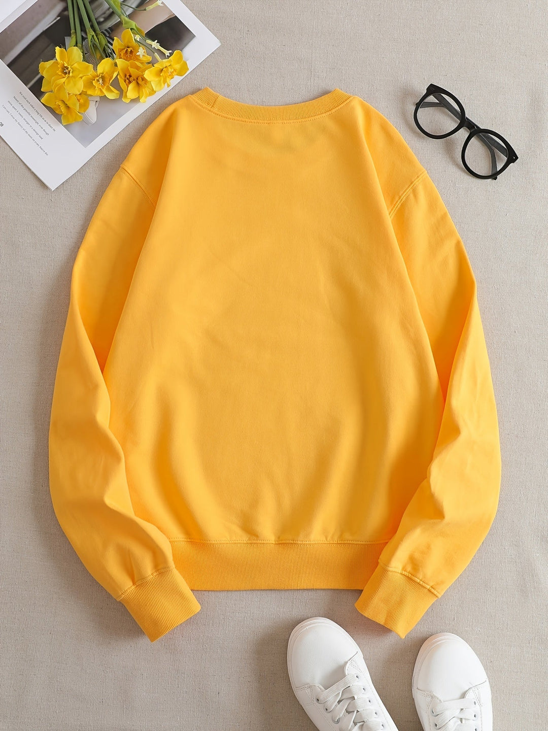 Gelber Pullover aus Baumwolle, lässig, auf Tisch mit Brille und gelben Blumen.