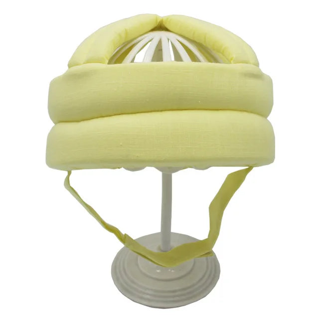 Gelber Baby-Schutzhelm aus Baumwolle auf weißem Ständer, ideal für Kleinkind-Sicherheit.