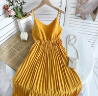 Gelbes Sommerkleid aus Satin mit Plissee, auf Tisch mit Perlenhandtasche und Blumen.