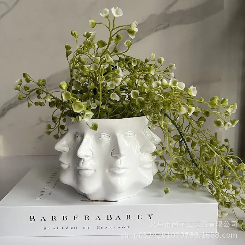 Weiße Gesichtsblumentopf-Vase mit grünen Kunstpflanzen auf Barbera-Buch.
