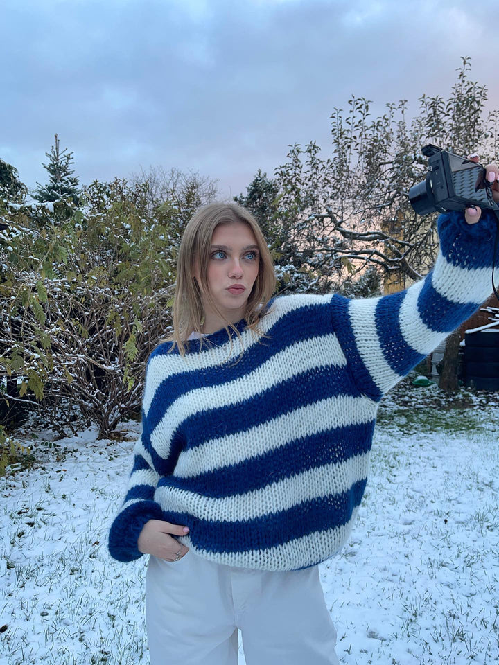 Frau im gestreiften Pullover macht Selfie im verschneiten Garten, Wintermode, blau-weiß gestreift.