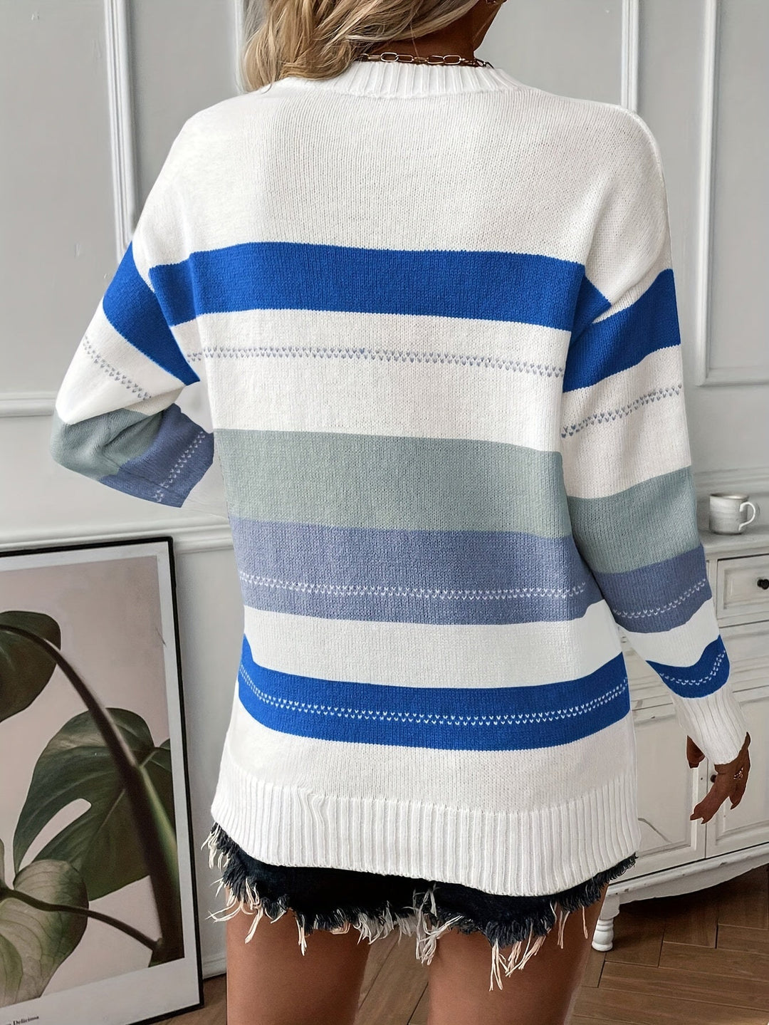 Frau in gestreiftem Pullover, blau-weiß, lässig, modisch, vor Wand mit Pflanzenbild.