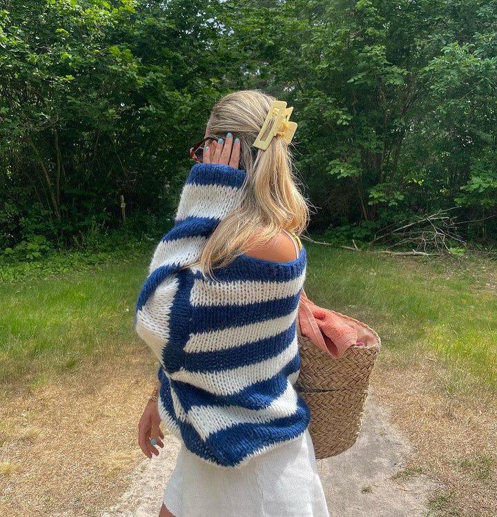Frau im gestreiften Pullover, blau-weiß, mit Strohtasche im Grünen, Sommermode.