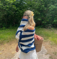 Frau im gestreiften Pullover, blau-weiß, mit Strohtasche im Grünen, Sommermode.