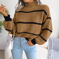 Frau in gestreiftem Strickpullover, beige mit schwarzen Streifen, hält weiße Handtasche.