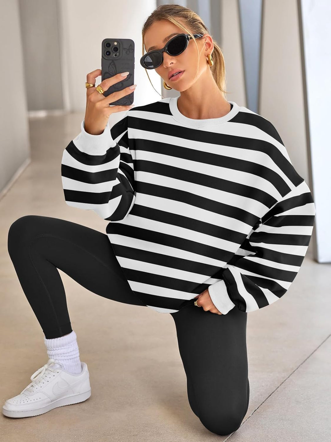 Frau in schwarz-weiß gestreiftem Pullover, schwarze Leggings, Sonnenbrille, kniet auf Boden.