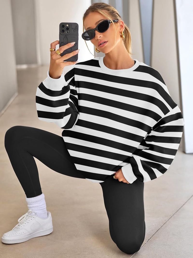 Frau in schwarz-weiß gestreiftem Pullover, schwarze Leggings, Sonnenbrille, kniet auf Boden.