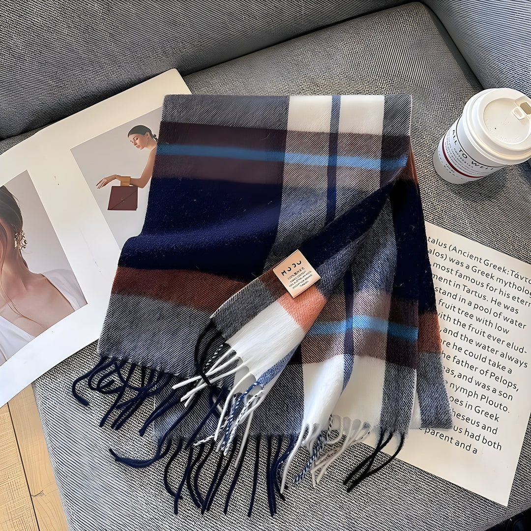 Gestreifter Wollschal in Blau, Weiß und Braun auf grauem Sofa, neben Kaffeebecher und Magazin.