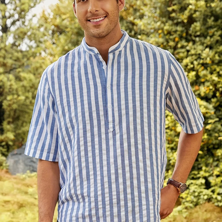 Mann in blau-weiß gestreiftem Hemd, Stehkragen, Kurzarm, lächelnd im Freien.