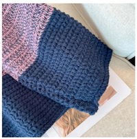 Gehäkelte Decke in Blau und Rosa auf beigem Sofa, handgemacht, gemütlich, Wohnaccessoire.