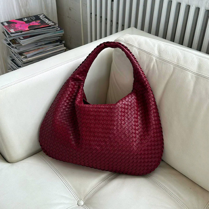 Rote geflochtene Handtasche aus Leder auf weißem Sofa, elegant und geräumig, ideal für Arbeit.