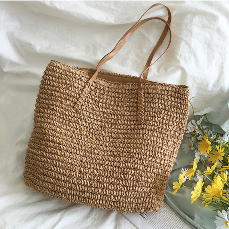 Braune Strohtasche mit Ledergriffen auf weißem Hintergrund, ideal für Sommer und Strand.