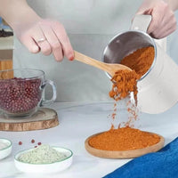 Frau gießt Gewürzpulver aus weißem Behälter auf Holzplatte, Küche, Kochen, Zutaten.