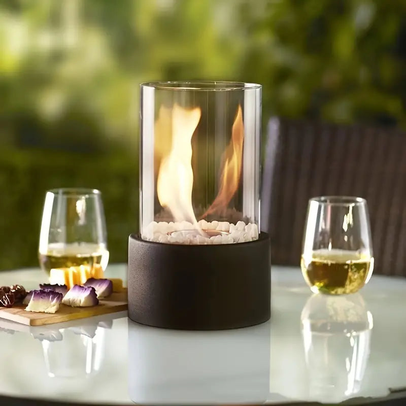 Glas-Feuerstelle auf Tisch, umgeben von Weingläsern und Snacks, ideal für Gartenabende.