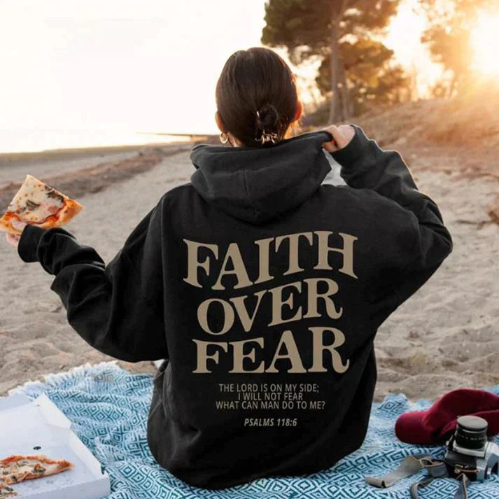 Frau am Strand mit schwarzem Hoodie "Faith Over Fear", Psalmen 118:6, christliche Mode.