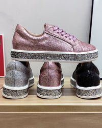 Glitzernde Sneaker in Rosa, Silber und Schwarz auf Holzregal, modische Damenschuhe.