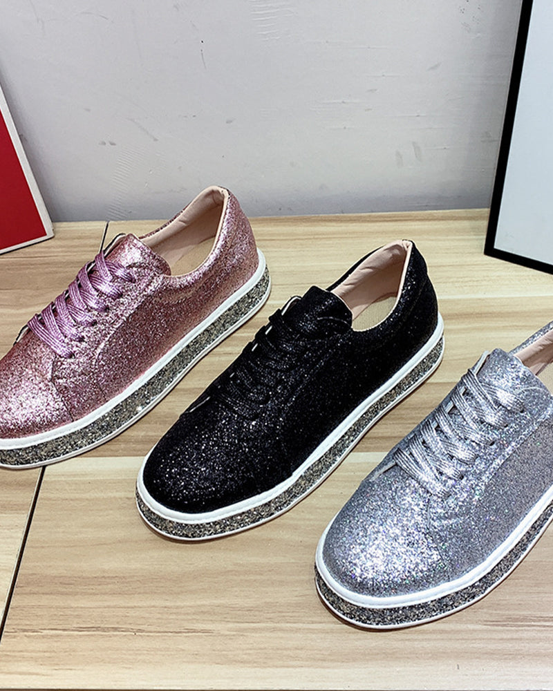 Drei glitzernde Sneaker in Rosa, Schwarz und Silber auf Holztisch, modische Damenschuhe.