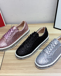 Drei glitzernde Sneaker in Rosa, Schwarz und Silber auf Holztisch, modische Damenschuhe.
