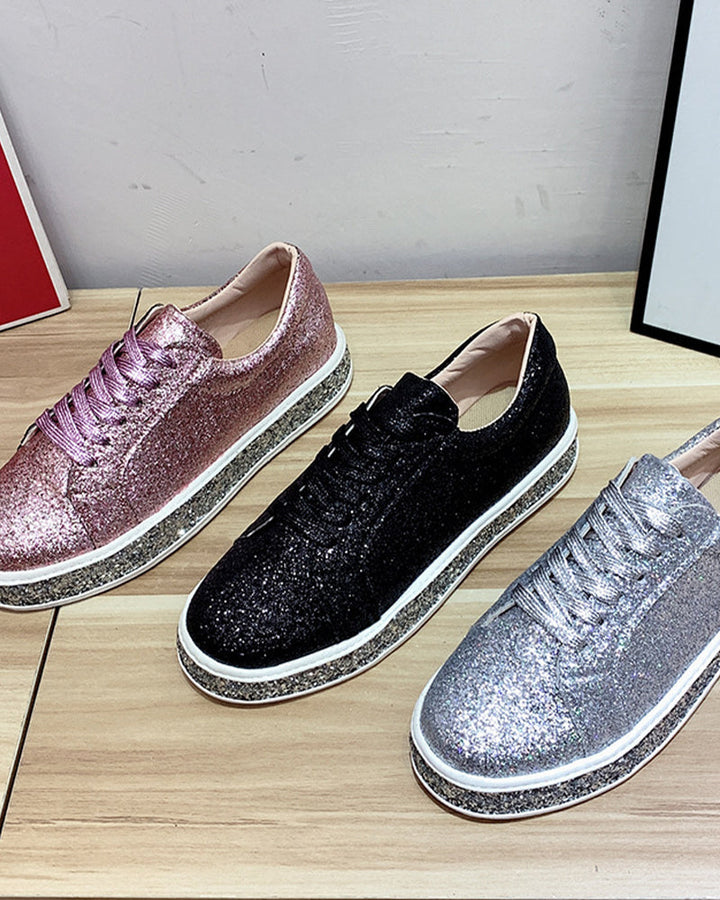 Drei glitzernde Sneaker in Rosa, Schwarz und Silber auf Holztisch, modische Damenschuhe.