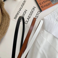 Drei schmale Ledergürtel in Schwarz, Braun und Weiß auf weißem Hintergrund, modisch, elegant.