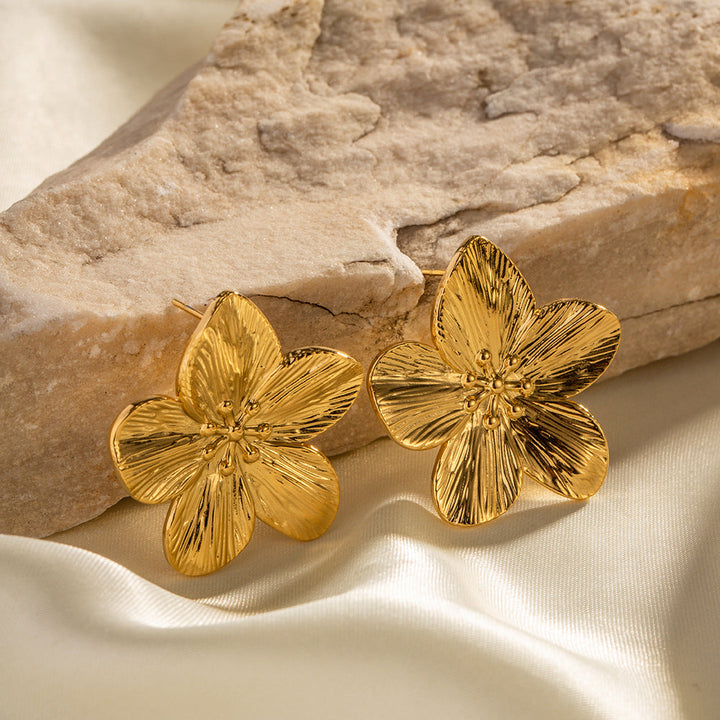 Goldene Blumen-Ohrringe auf beigem Stein, eleganter Schmuck, modische Accessoires.