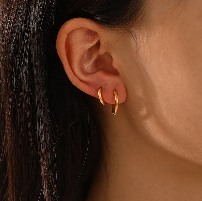 Goldene Creolen-Ohrringe an Ohr, eleganter Schmuck, modisches Accessoire, Damenmode.