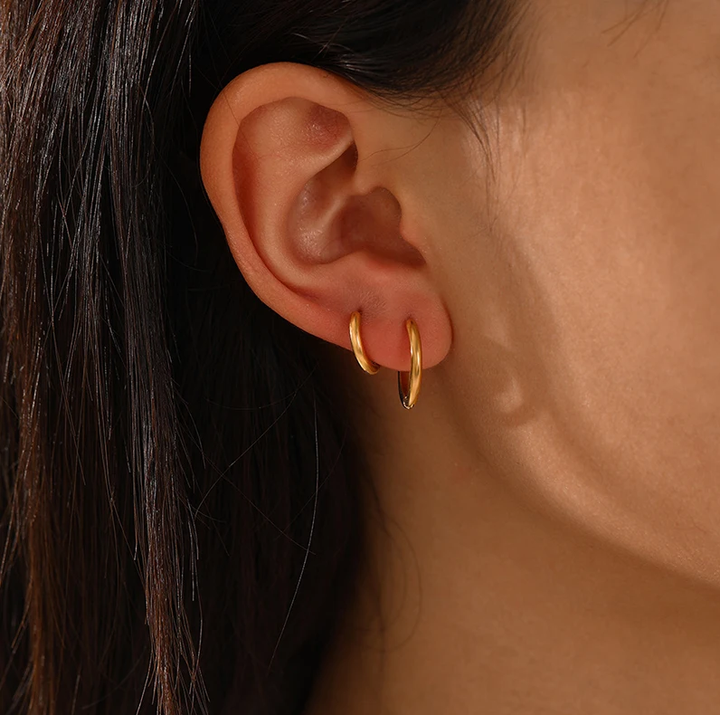 Goldene Creolen-Ohrringe an Ohr, eleganter Schmuck, modisches Accessoire, Damenmode.