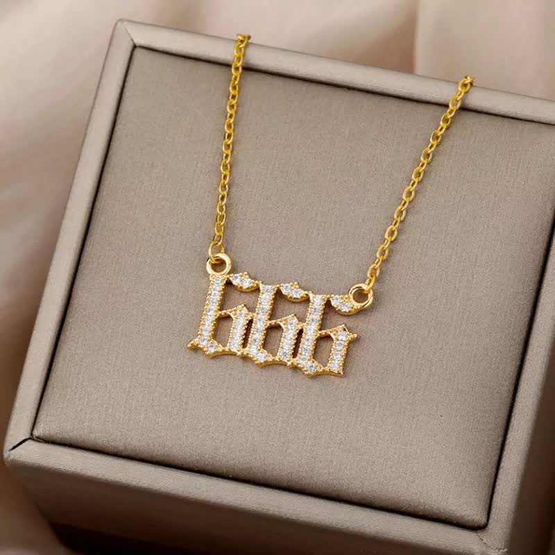 Goldene Halskette mit "666"-Anhänger, verziert mit Diamanten, auf beigem Schmuckkästchen.