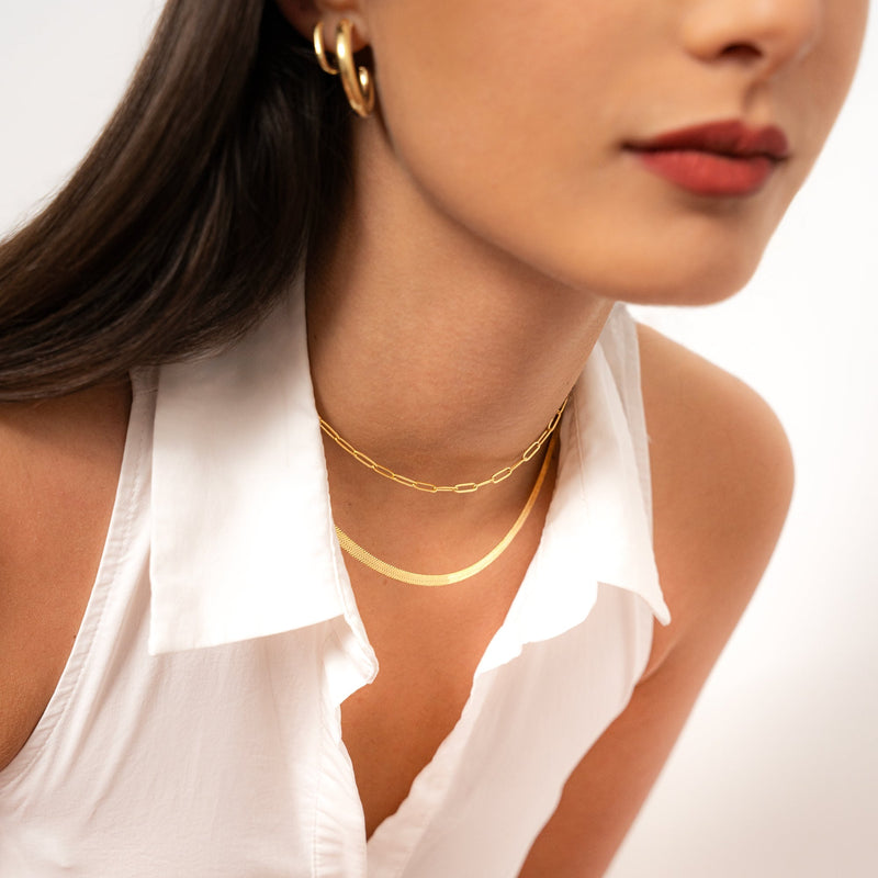 Frau mit goldener Halskette und Ohrringen, weißes Hemd, eleganter Schmuck, Modeaccessoires.