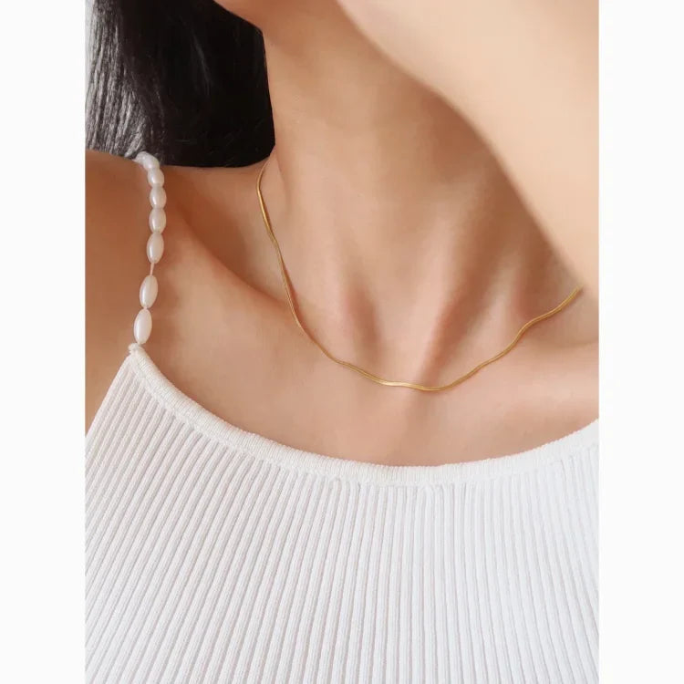 Frau trägt goldene Halskette und weißes geripptes Top, eleganter Schmuck, minimalistisch.