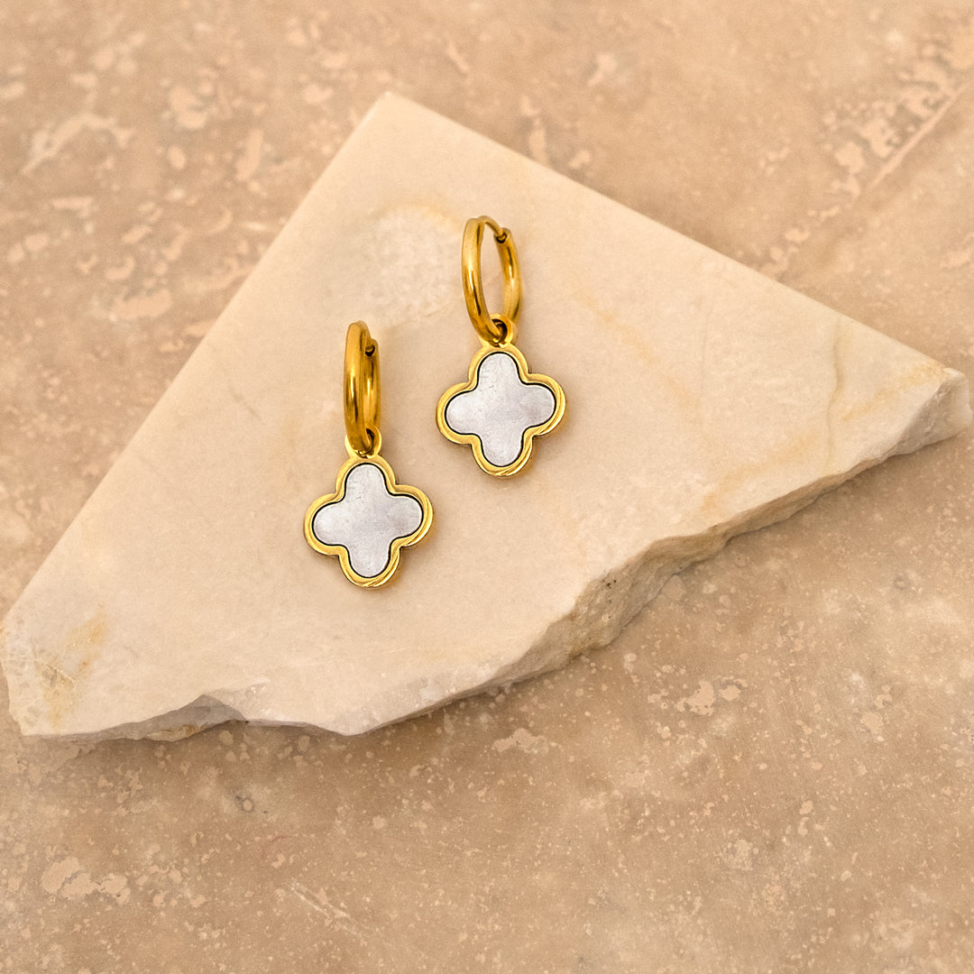Goldene Kleeblatt-Ohrringe mit Muschel-Design auf Marmorhintergrund.
