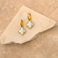 Goldene Kleeblatt-Ohrringe mit Muschel-Design auf Marmorhintergrund.