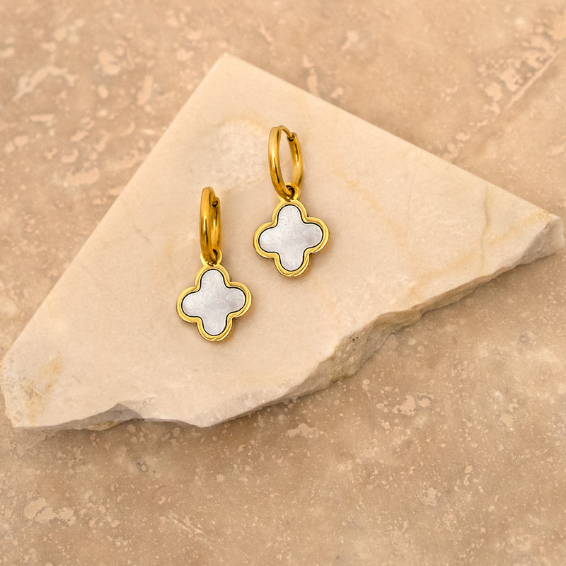 Goldene Kleeblatt-Ohrringe mit Muschel-Design auf Marmorhintergrund.