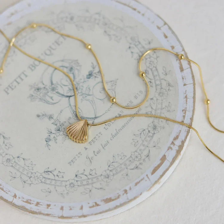 Goldene Muschelkette auf Vintage-Teller, eleganter Schmuck, maritimes Design, Damenaccessoire.