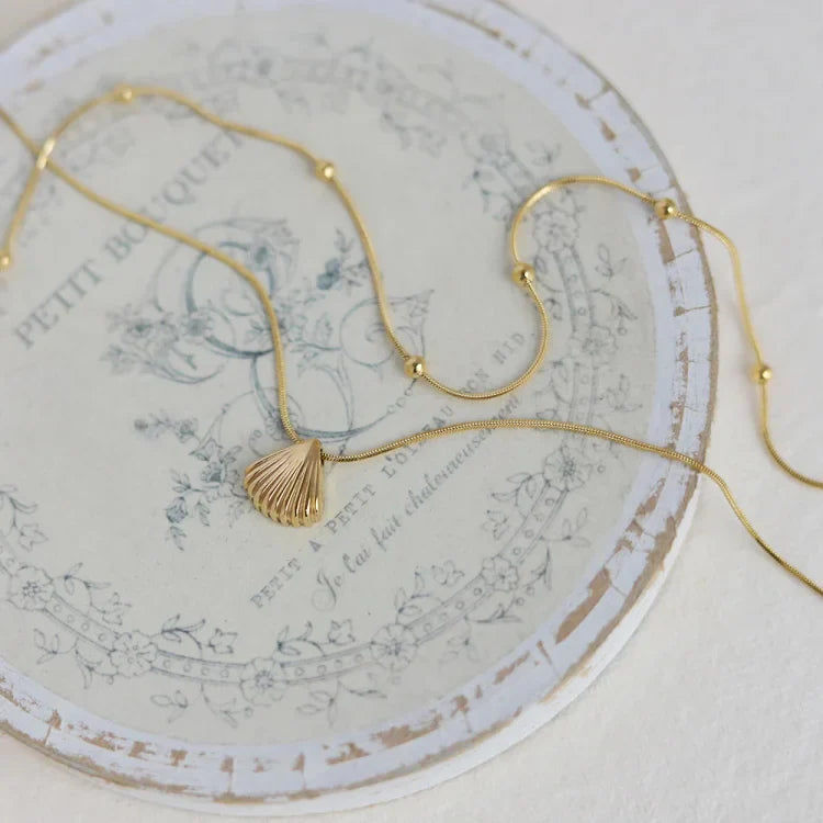 Goldene Muschelkette auf Vintage-Teller, eleganter Schmuck, maritimes Design, Damenaccessoire.