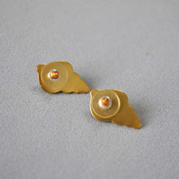 Goldene Flügel-Ohrringe mit orangefarbenem Stein auf grauem Hintergrund, modischer Schmuck.