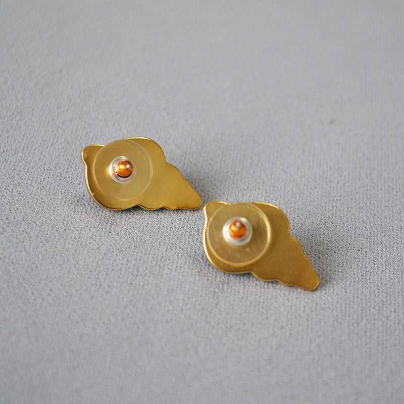 Goldene Flügel-Ohrringe mit orangefarbenem Stein auf grauem Hintergrund, modischer Schmuck.