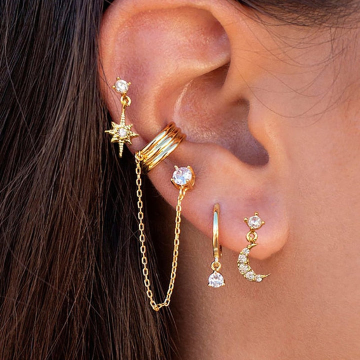 Frauenohr mit goldenen Ohrringen, Stern- und Monddesign, modischer Schmuck, Piercing-Trend.
