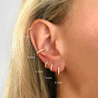 Frauenohr mit mehreren goldenen Ohrringen, Größenangaben, modischer Schmuck, Nahaufnahme.