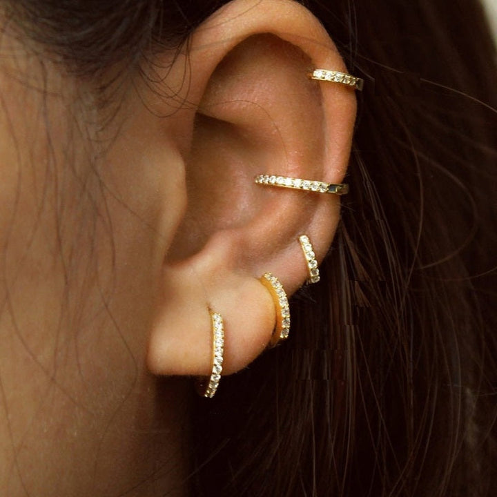 Fünf goldene Ohrmanschetten mit Strasssteinen an einem Ohr, modischer Ohrschmuck.