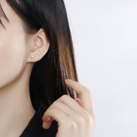 Frau mit goldenen Ohrsteckern, quadratisches Design, eleganter Schmuck, Nahaufnahme.