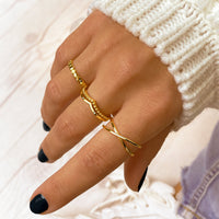 Hand mit goldenen Ringen, weißer Strickpullover, schwarze Nägel, modisches Accessoire.