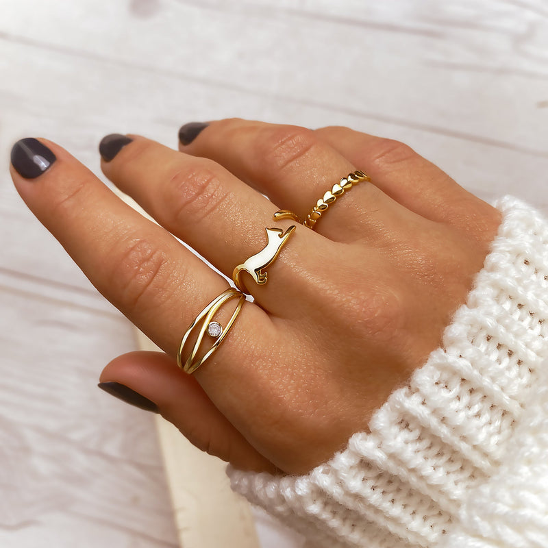Damenhand mit drei goldenen Ringen, darunter ein Katzenring, auf weißem Hintergrund.