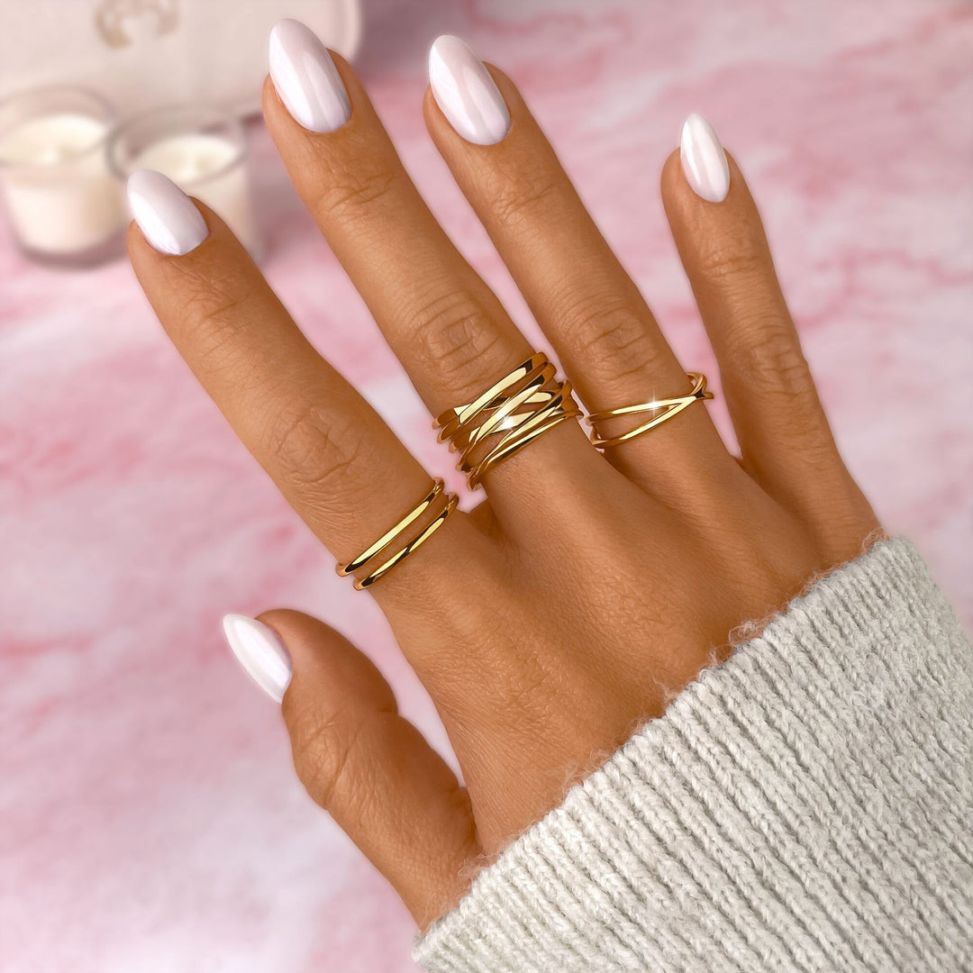Damenhand mit goldenen Ringen, weißer Nagellack, rosa Hintergrund, eleganter Schmuck.